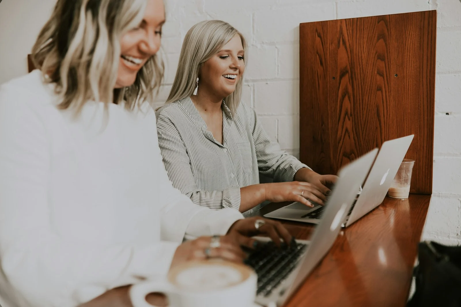 Two women working on laptops at a wooden café counter