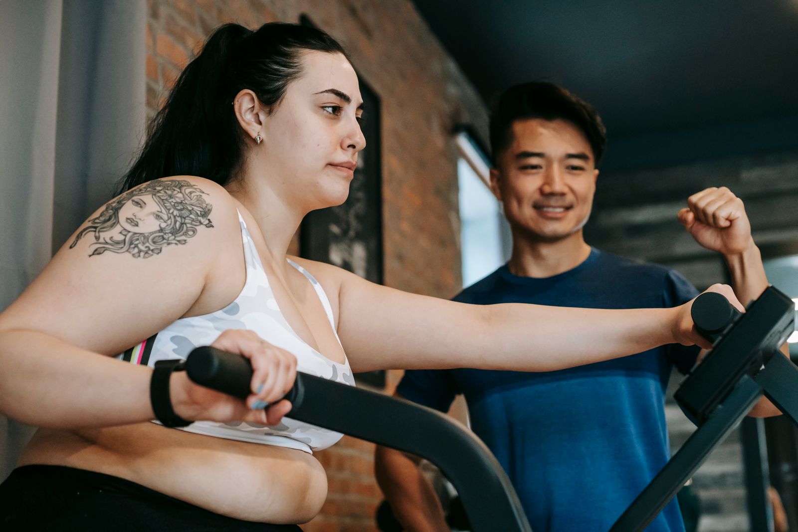 Trainer guiding a woman on an elliptical machine.