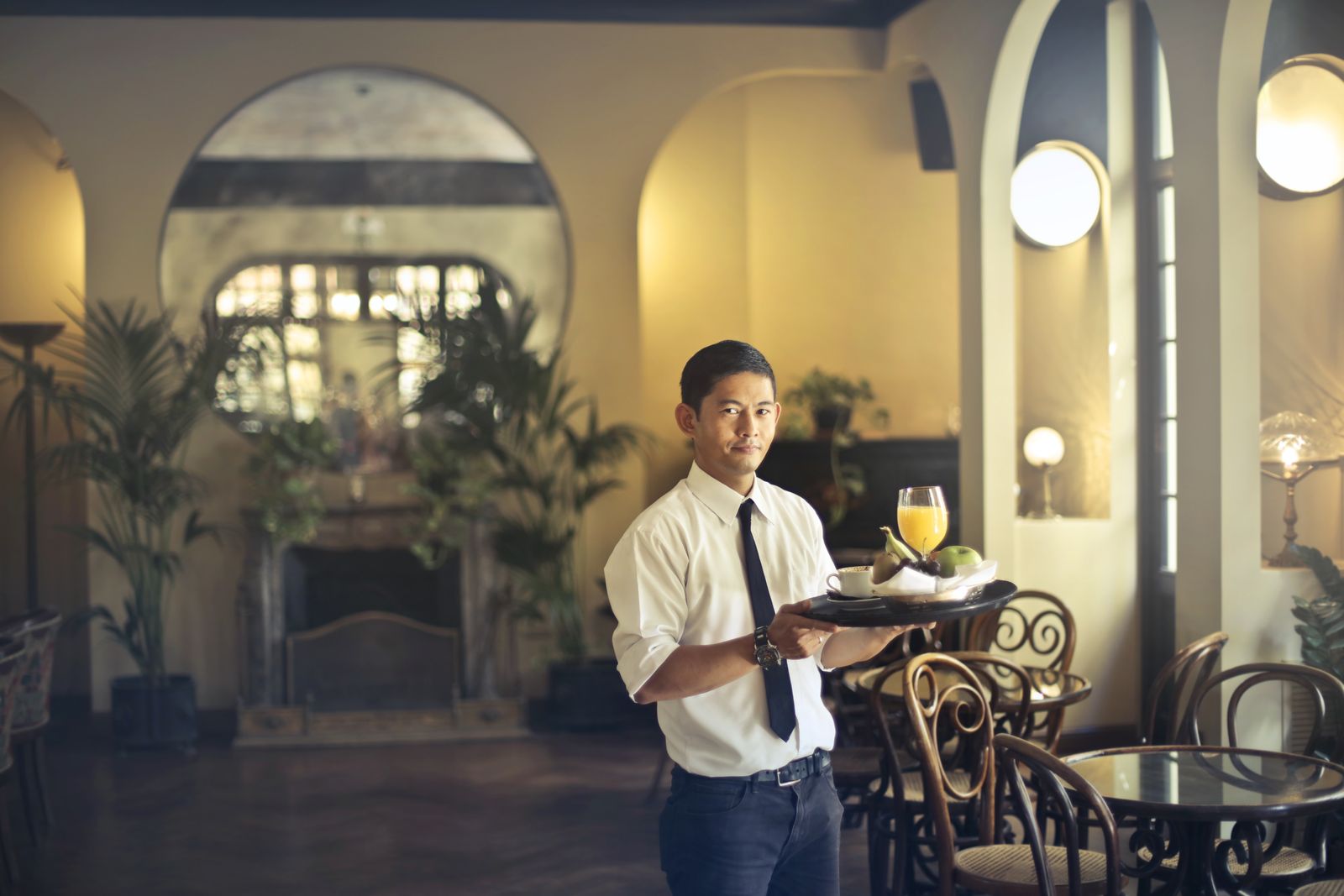Waiter with a tray inside a warm, lived-in restaurant.