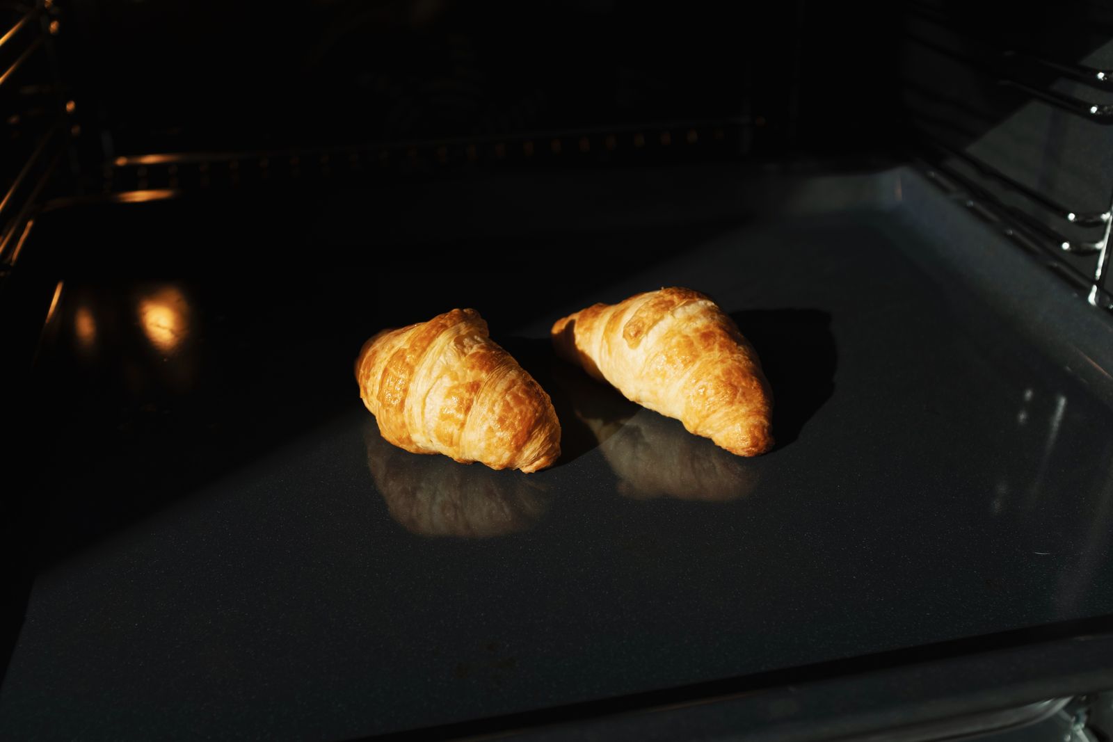 Two golden croissants on a baking tray in an oven.