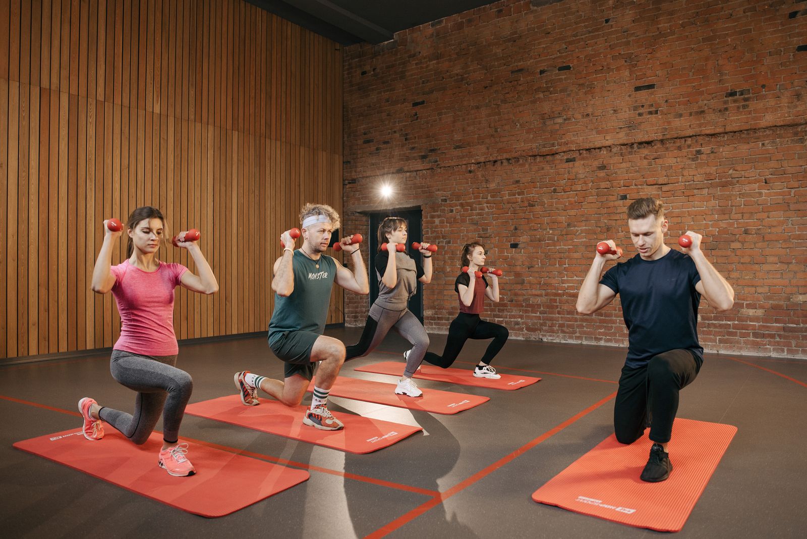 Adults exercising together with dumbbells on studio mats.