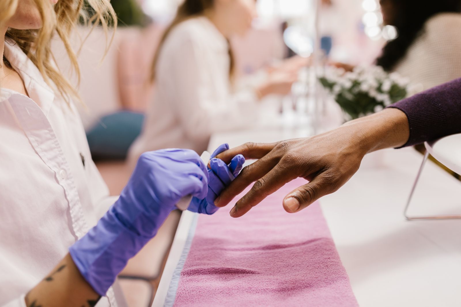 A gloved manicurist filing a client’s nails at a salon table.