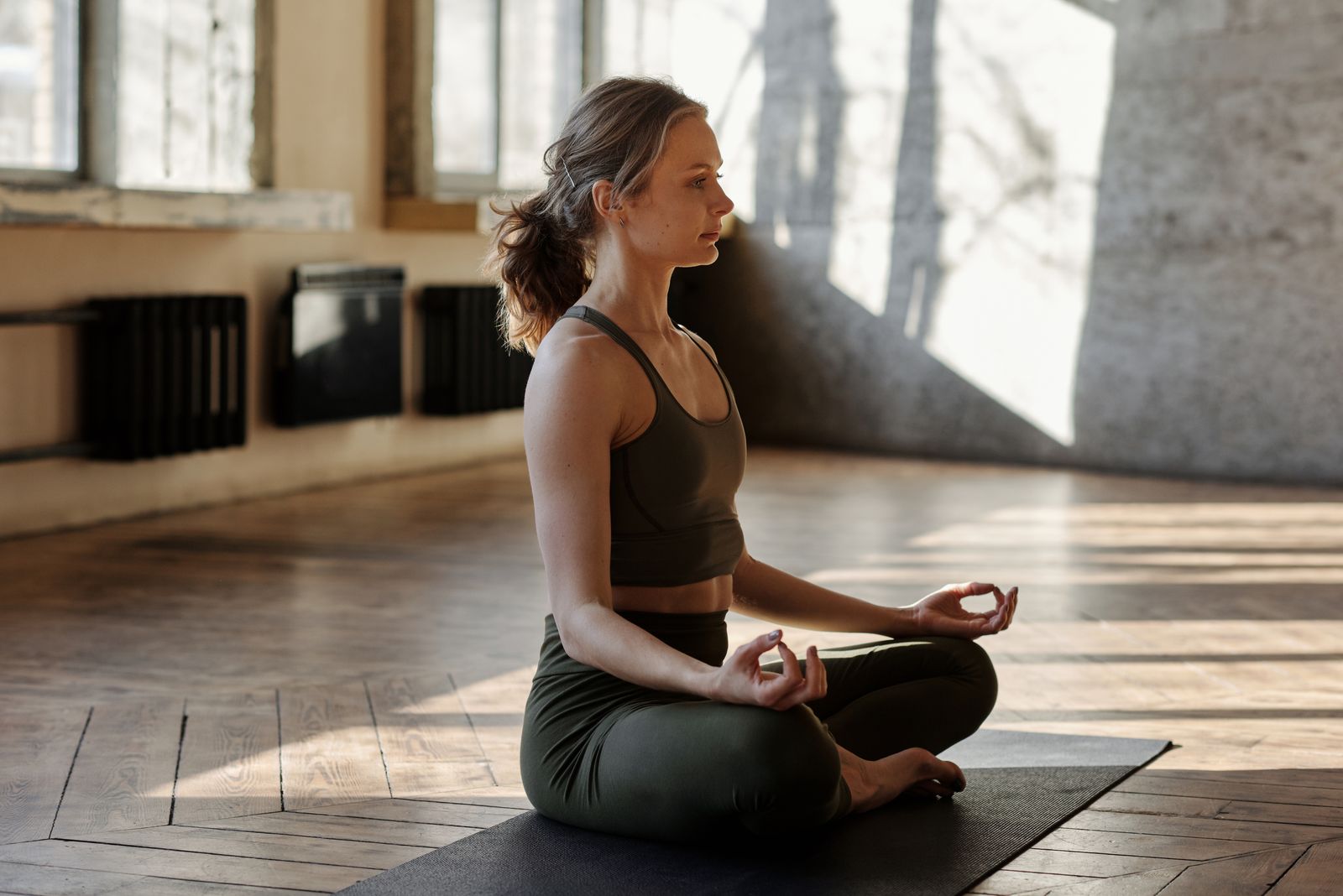 A woman meditating on a mat in a naturally lit studio.